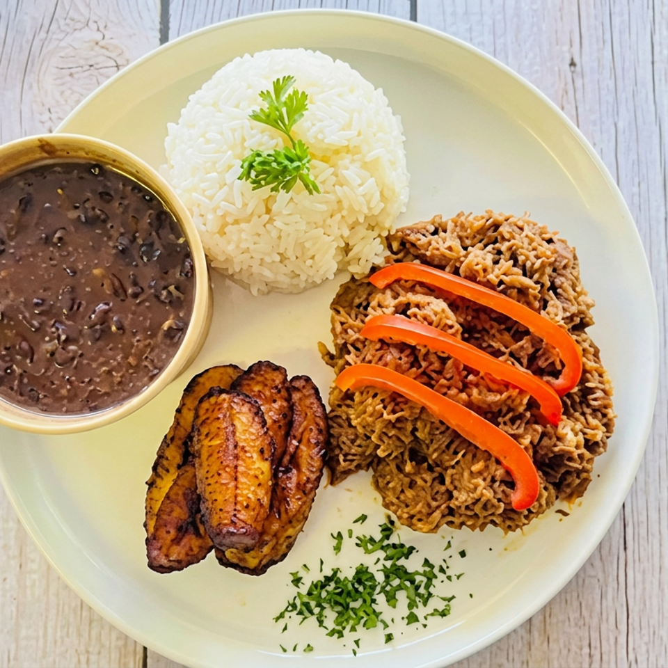 Plate of white rice, black beans, fried plantains, and shredded meat topped with red pepper strips and parsley.