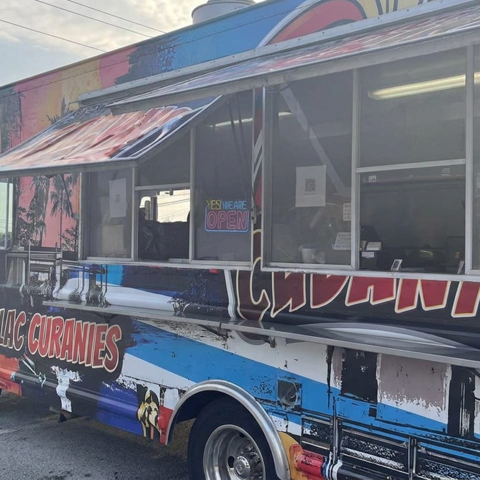 Colorfully painted food truck labeled LLC Curbannas parked outdoors, with service windows, open sign, and delivery pickup signage.